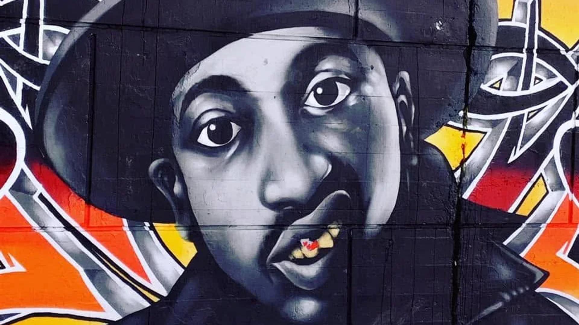 Mural portrait of a grayscale man in a fedora, with a red maple leaf on a gold tooth, against colorful graffiti, Centretown, Ottawa.