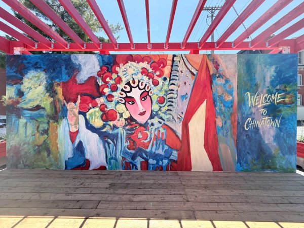 Graphic mural featuring the text "Welcome to Chinatown" in elegant gold lettering alongside an artistic painting of a Chinese opera performer in a detailed red headdress.