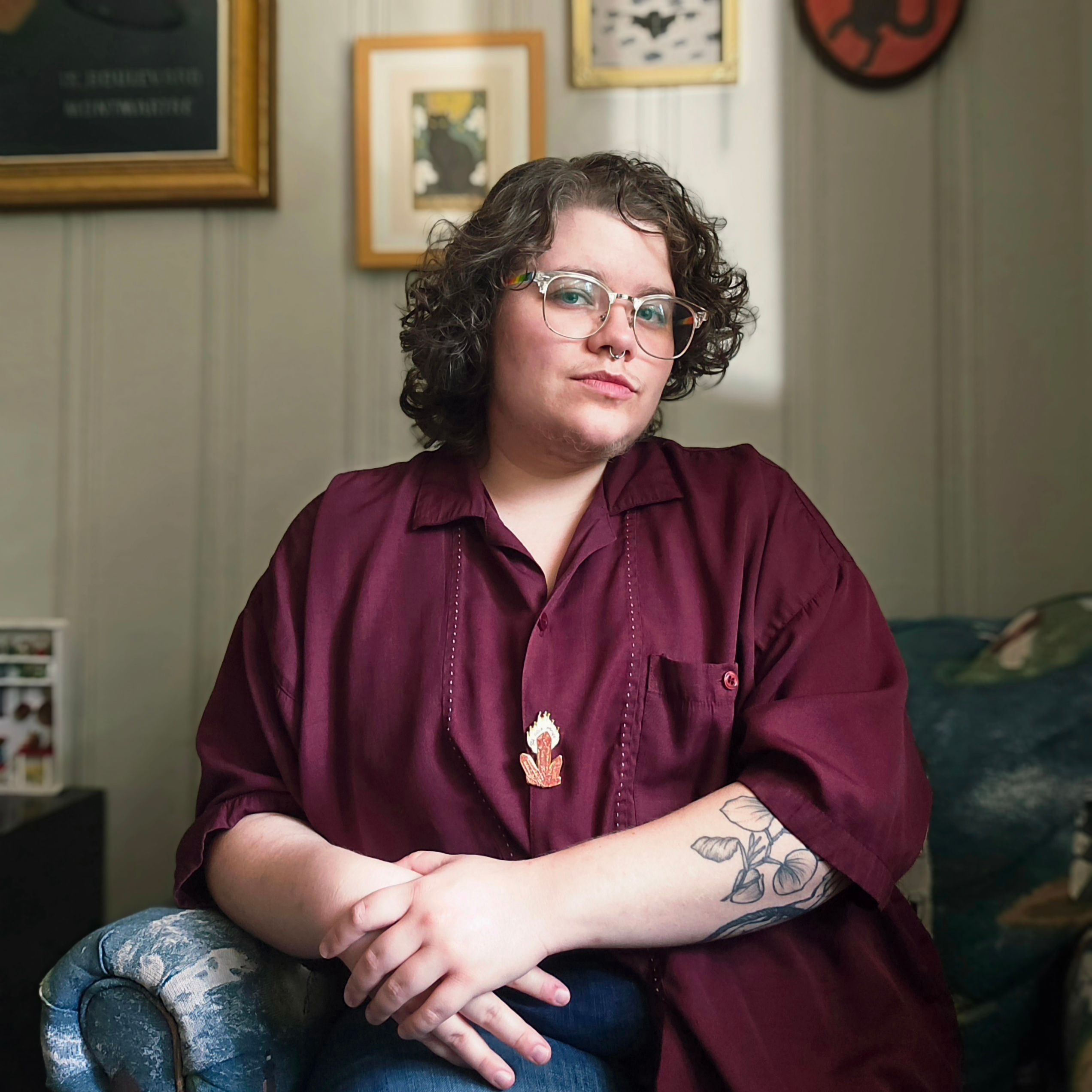 Vern in a maroon shirt sits in front of a gallery wall including art of cats and a cicada.