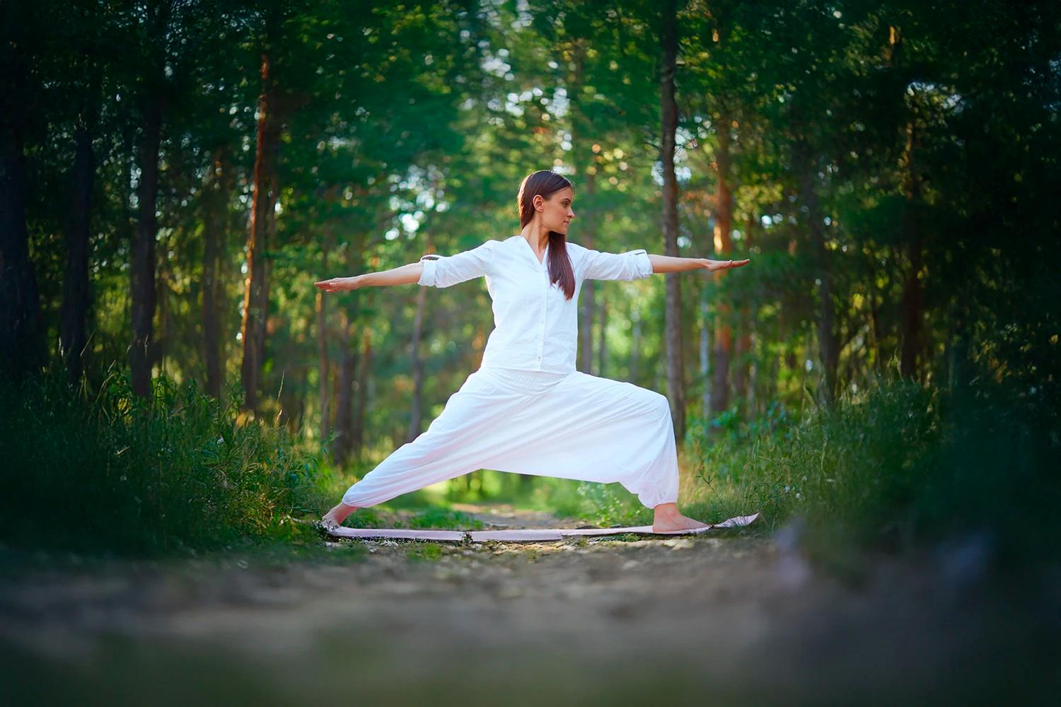 Una praticante in bianco in una posizione di Qi Gong in un bosco.