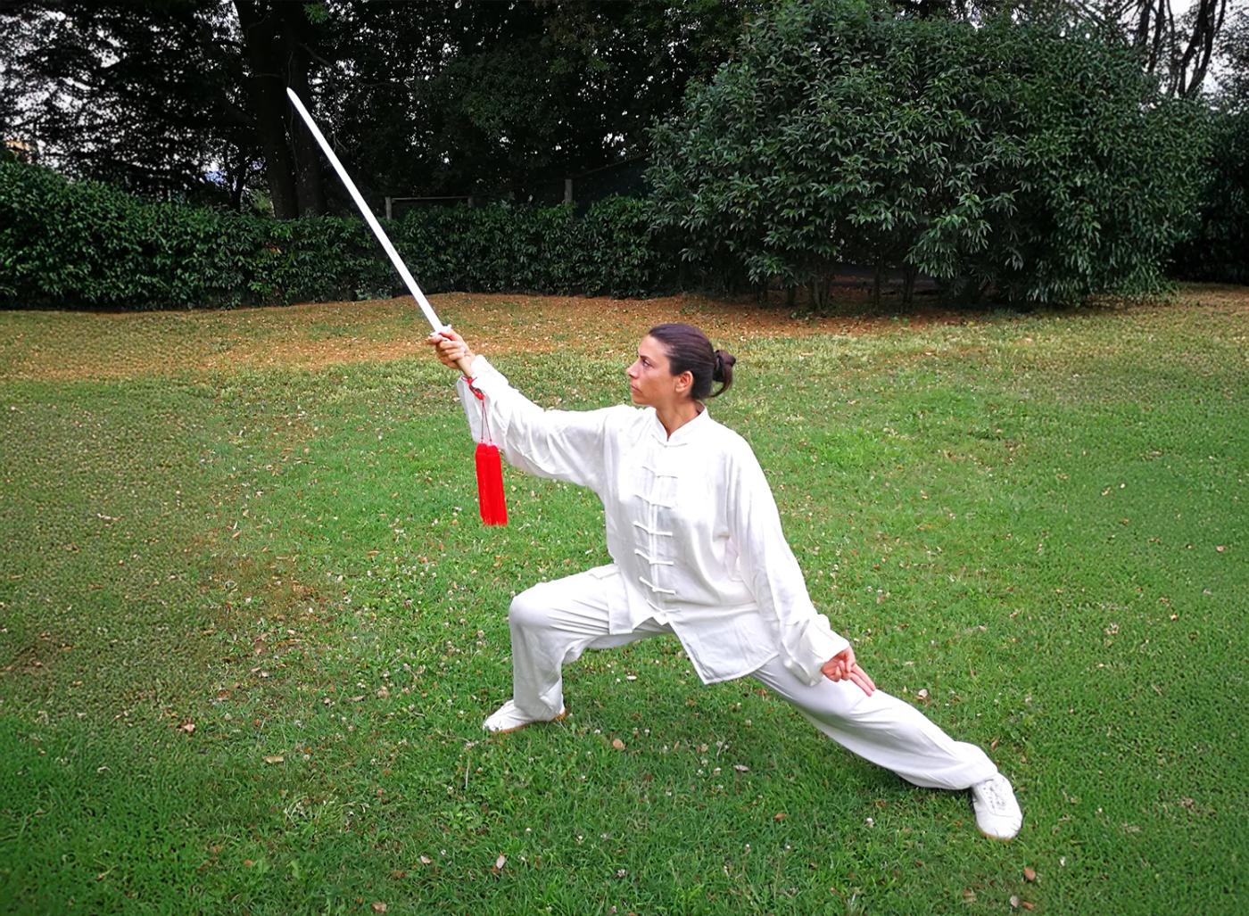Carolina Inda in una posizione di Taiji Quan con la spada in un giardino.