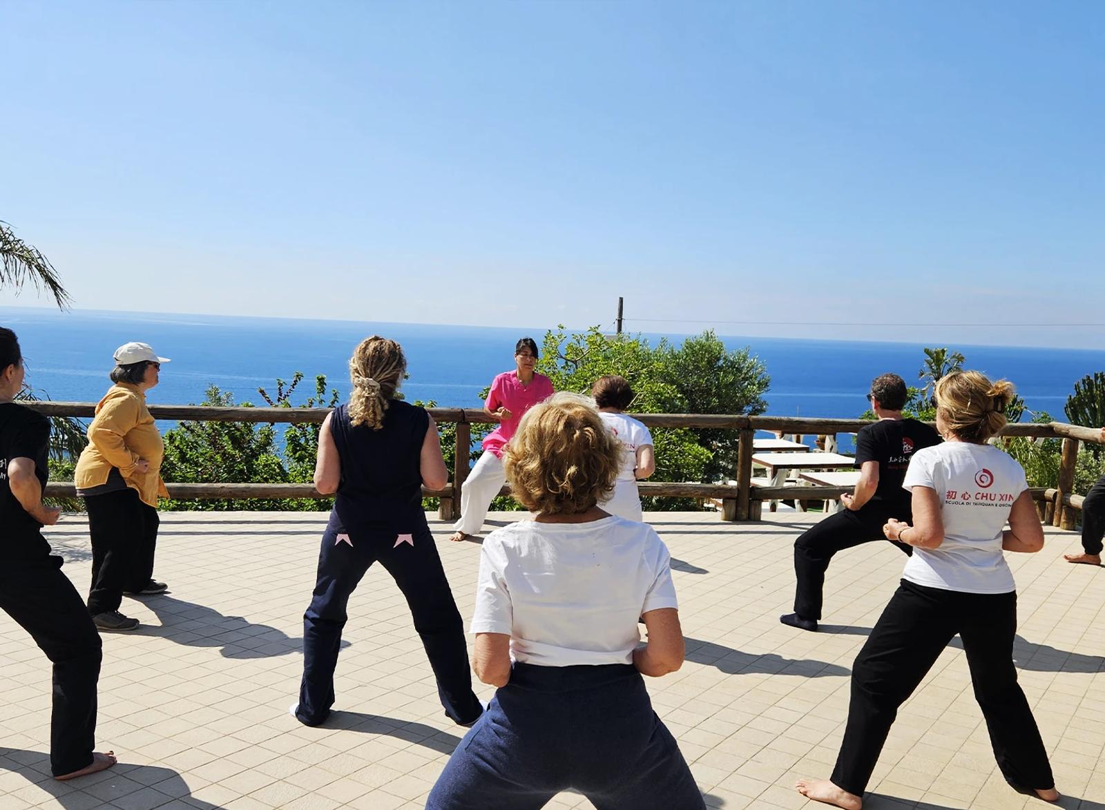 Un gruppo pratica Qi Gong all’aperto con Carolina Inda davanti al mare.