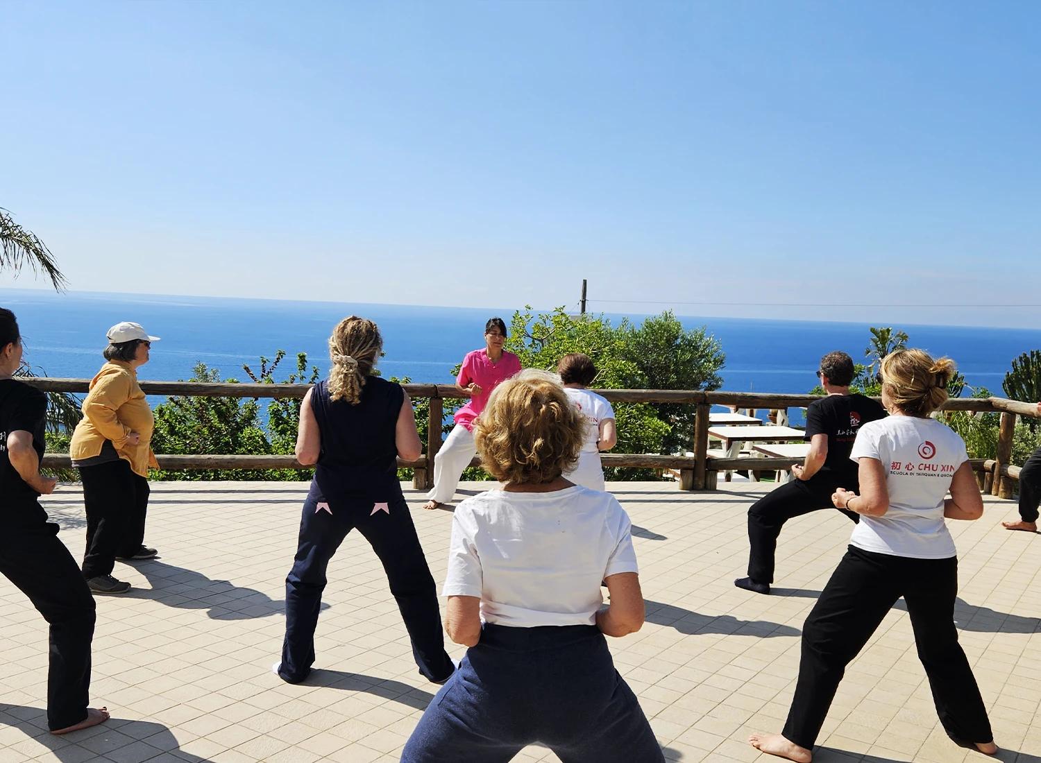 Un gruppo pratica Qi Gong all’aperto con Carolina Inda davanti al mare.