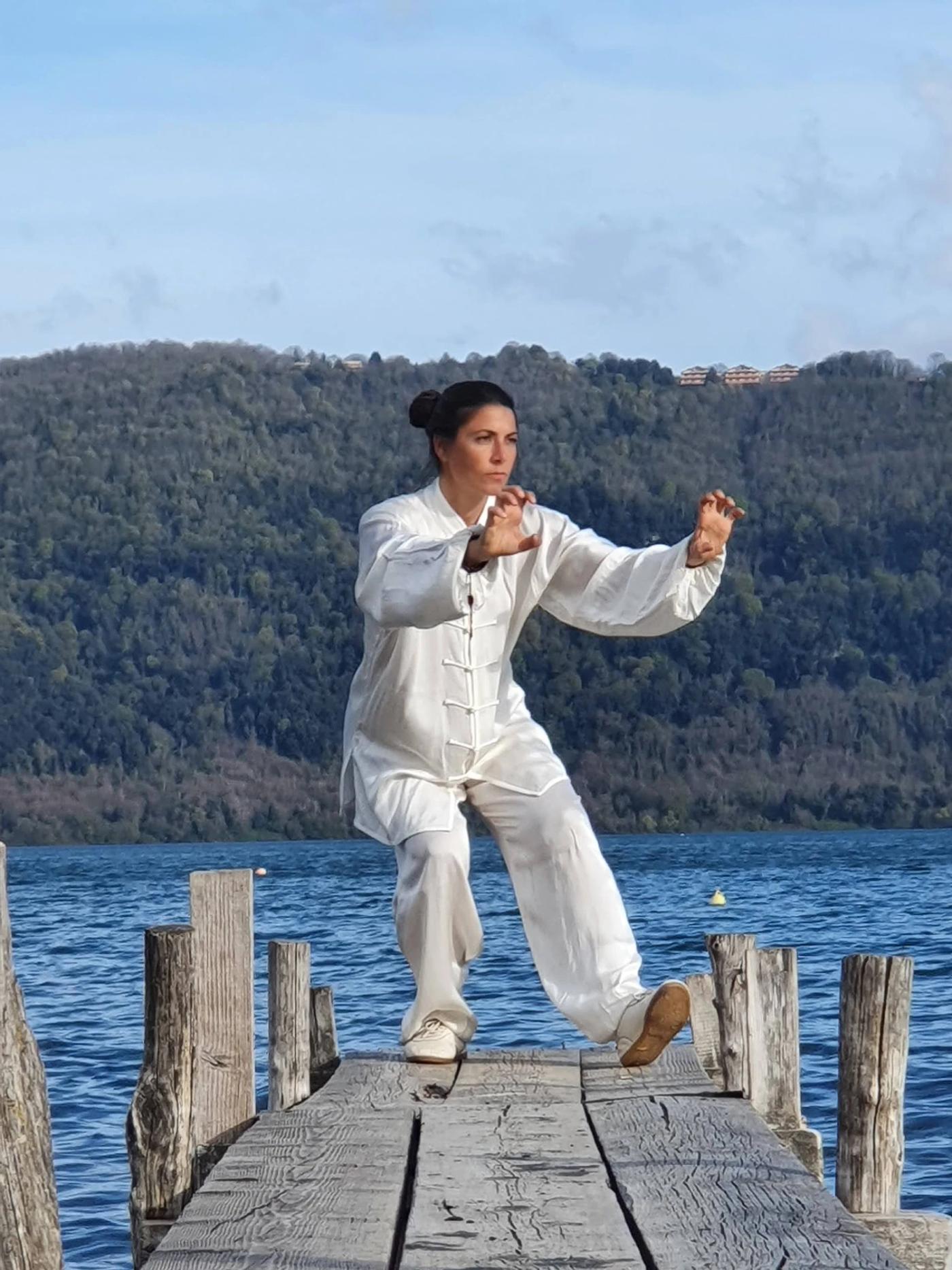 Carolina Inda esegue un movimento di Qi Gong su un pontile sul lago.
