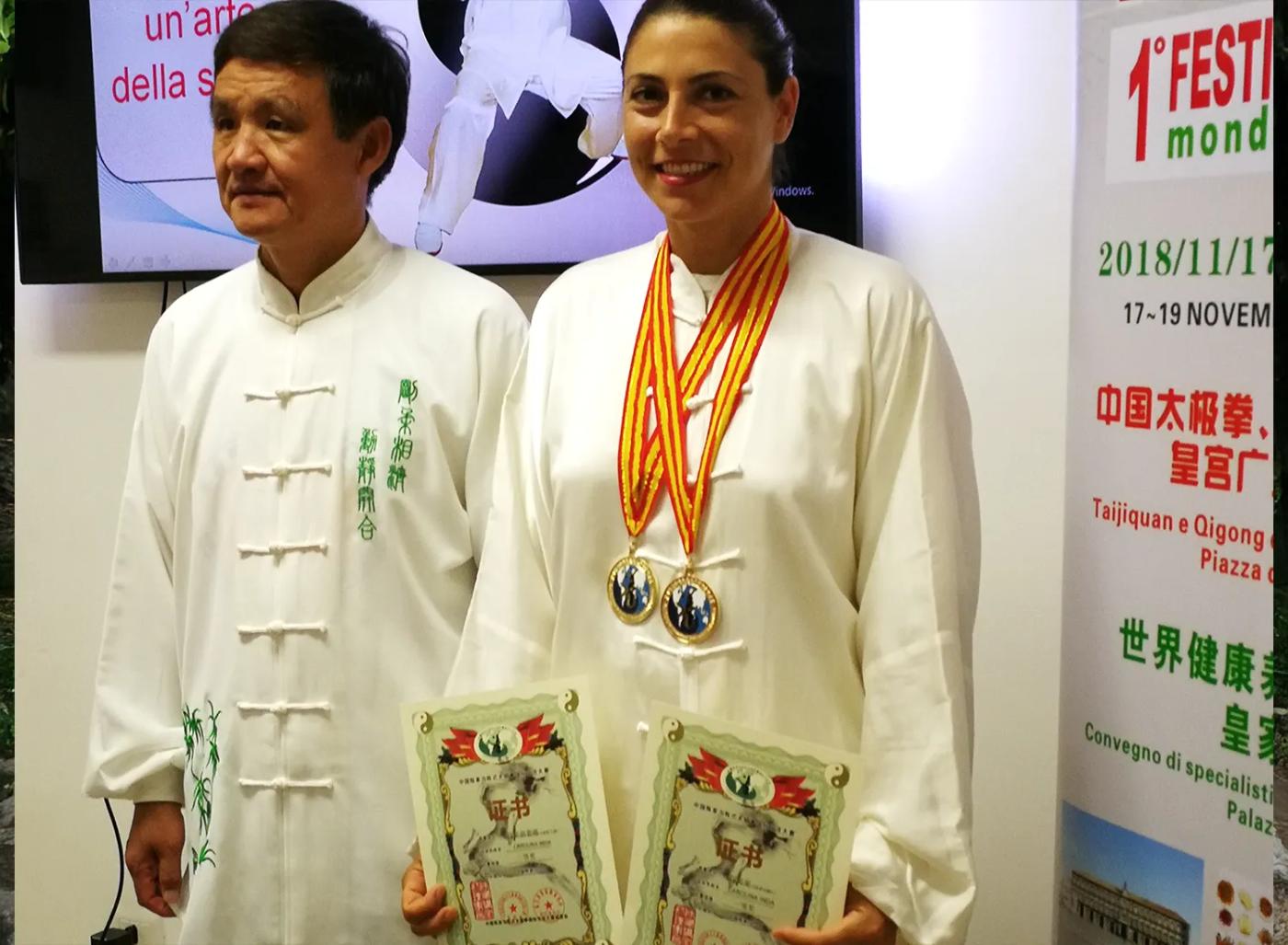 Carolina Inda con medaglie e diplomi accanto a un maestro in abito tradizionale.