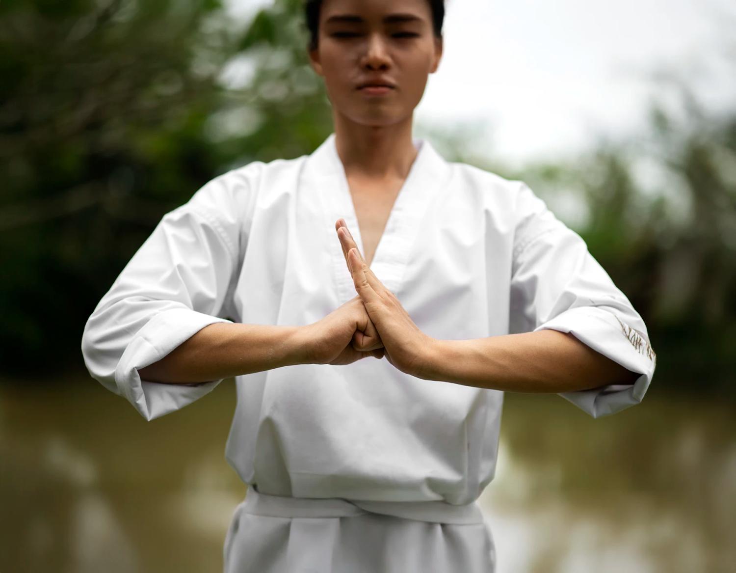 Una praticante in abito bianco unisce le mani in meditazione all’aperto.