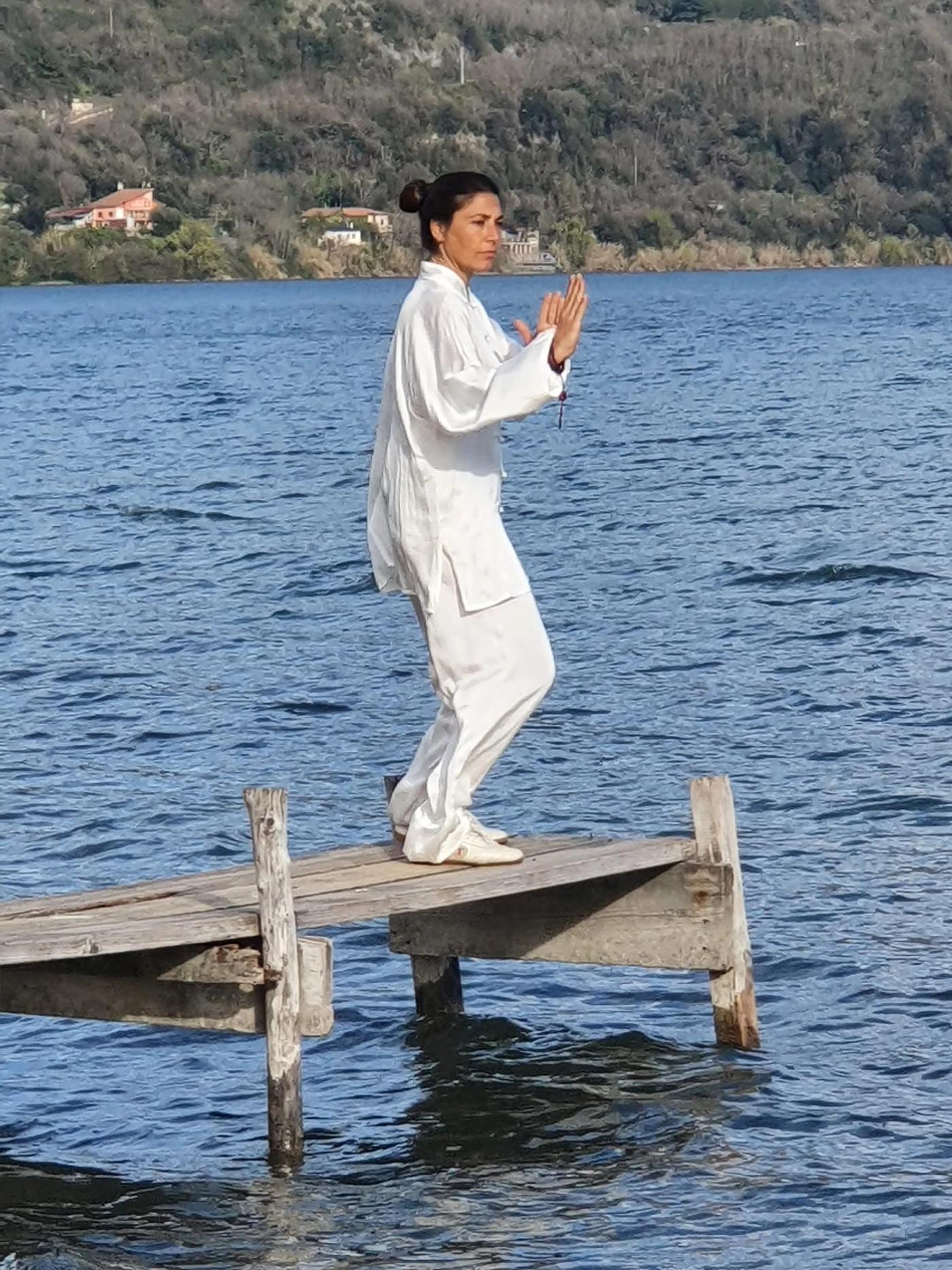 Carolina Inda in equilibrio su una gamba sul pontile, con il lago alle spalle.
