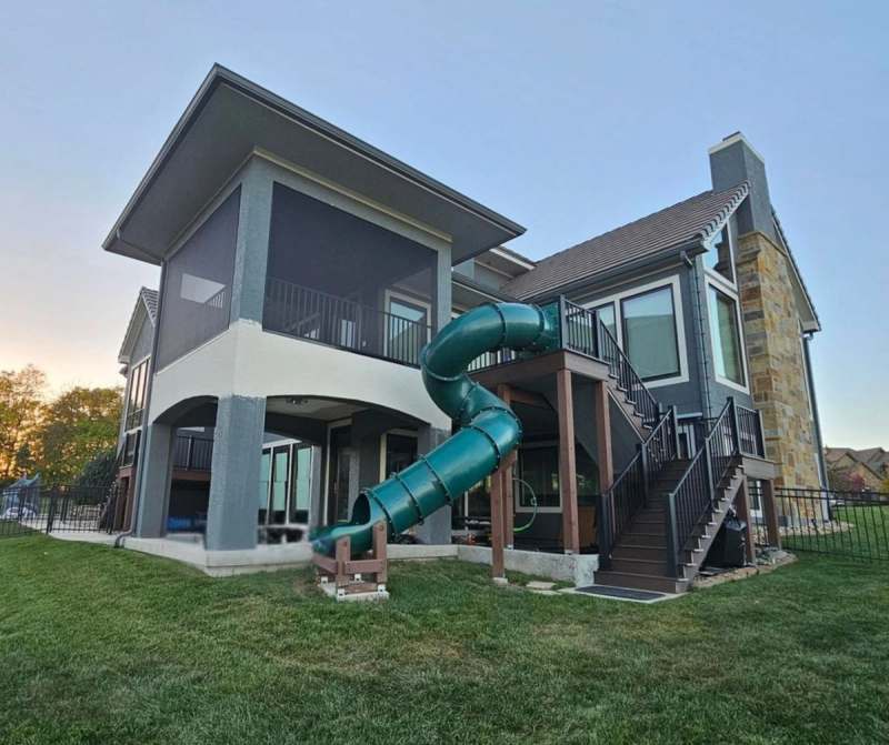 The finished deck, screened porch and slide seen from the lawn, with the stone chimney beyond