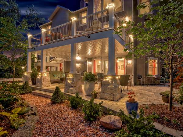 Outdoor living space by All Under One Roof at twilight with covered patio, stone columns, landscape lighting and paver patio, Kansas City