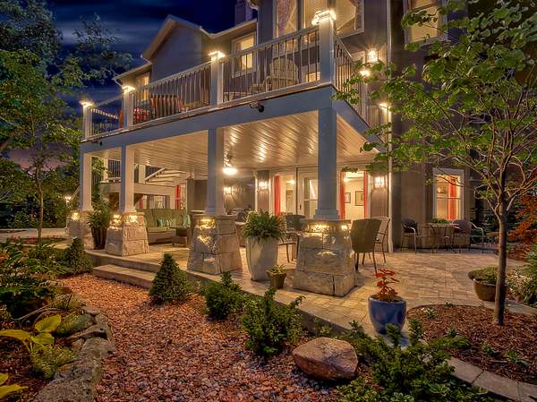 Outdoor living space by All Under One Roof at twilight with covered patio, stone columns, landscape lighting and paver patio, Kansas City