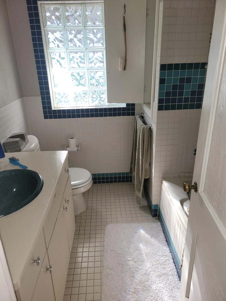 The hall bath before the remodel, with a single vanity, square floor tile & a glass block window