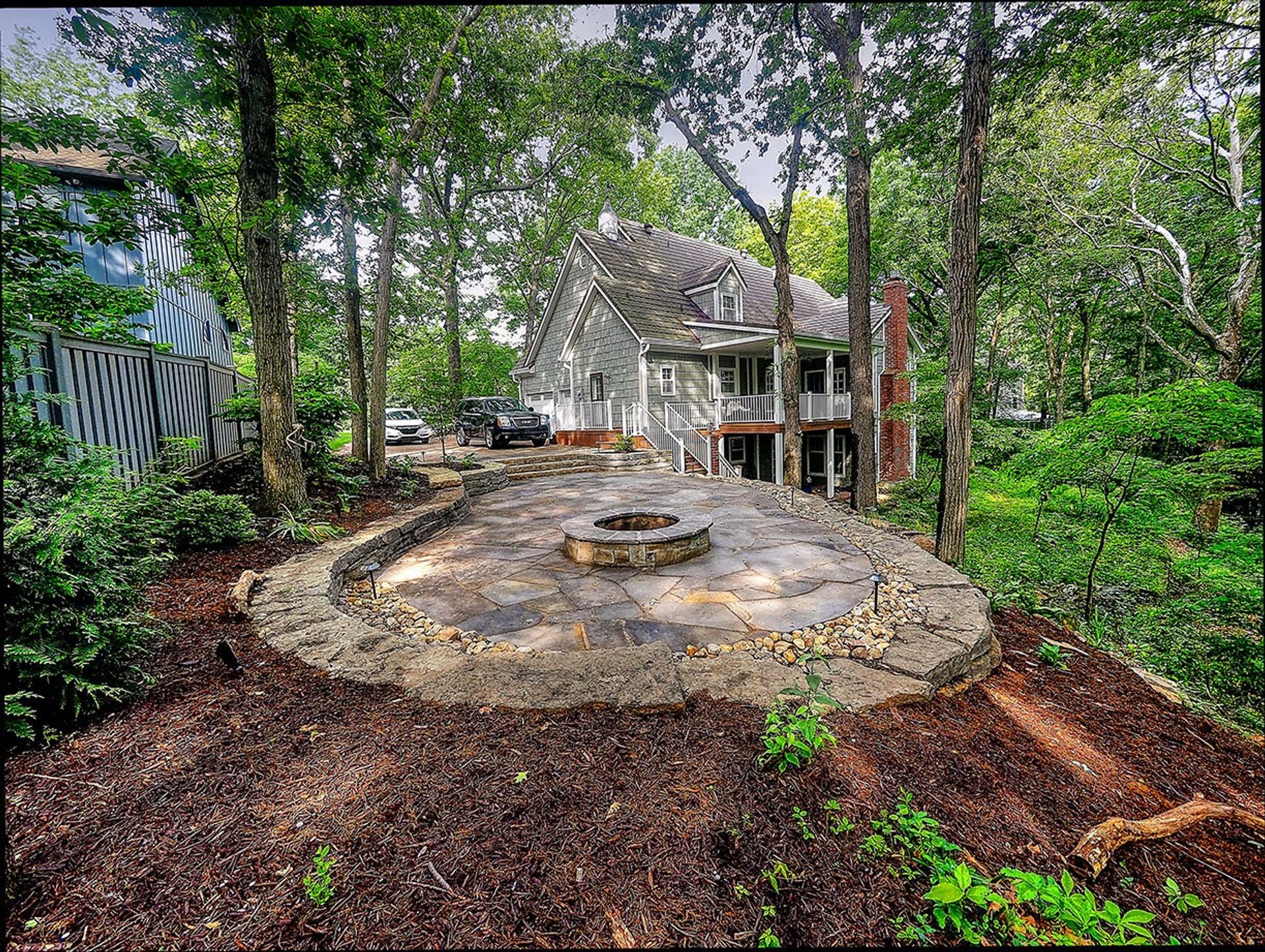The finished flagstone patio & stone fire pit in Overland Park, Kansas, held by dry stacked limestone walls, with the house beyond the trees