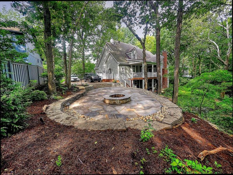 The finished flagstone patio & stone fire pit in Overland Park, Kansas, held by dry stacked limestone walls, with the house beyond the trees
