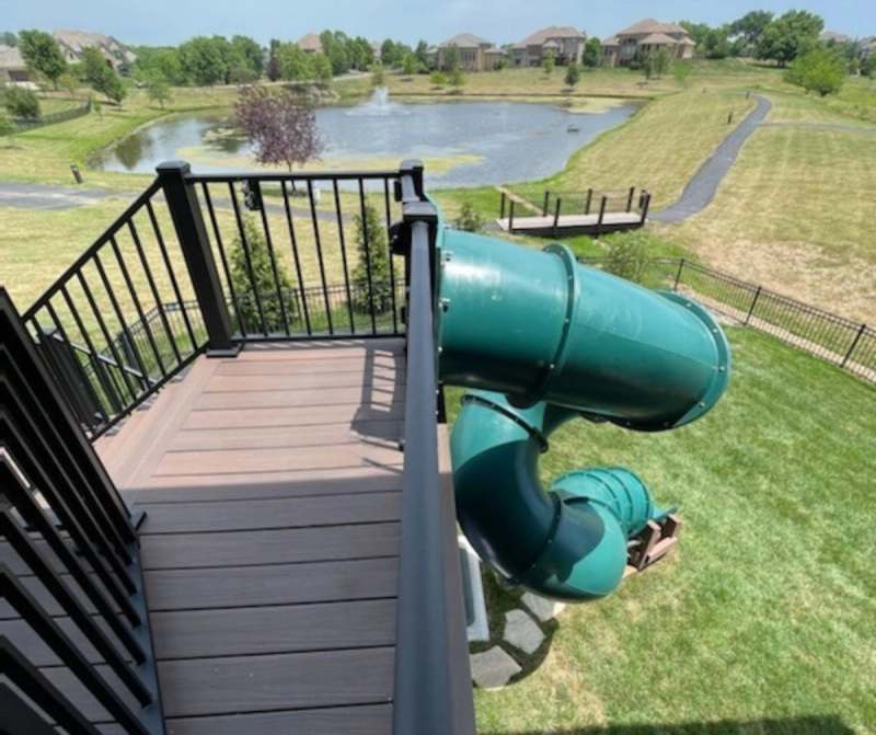 The finished deck boards & steel baluster rail, with the slide landing on the lawn & the pond beyond