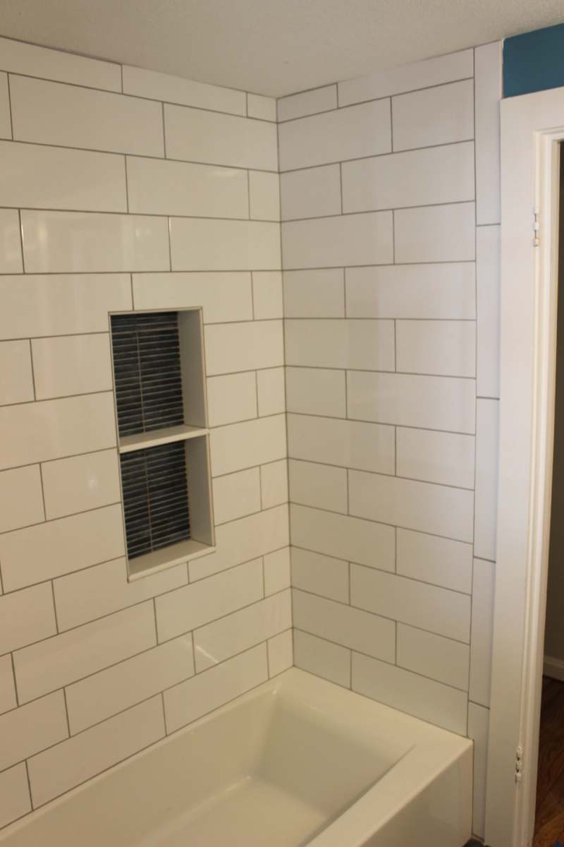 White subway tile running to the ceiling above the tub, with the tiled niche