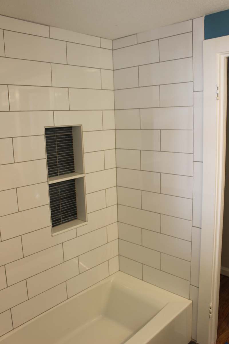 White subway tile running to the ceiling above the tub, with the tiled niche