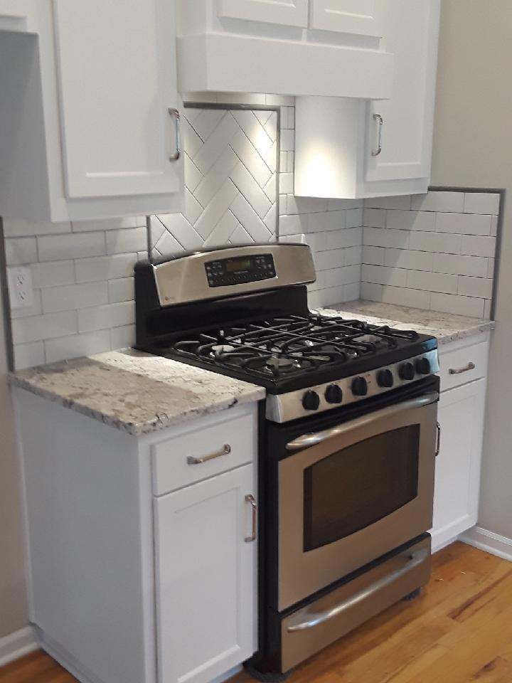 The rebuilt stove wall with new upper cabinets, a hood cabinet & a herringbone tile panel behind the range