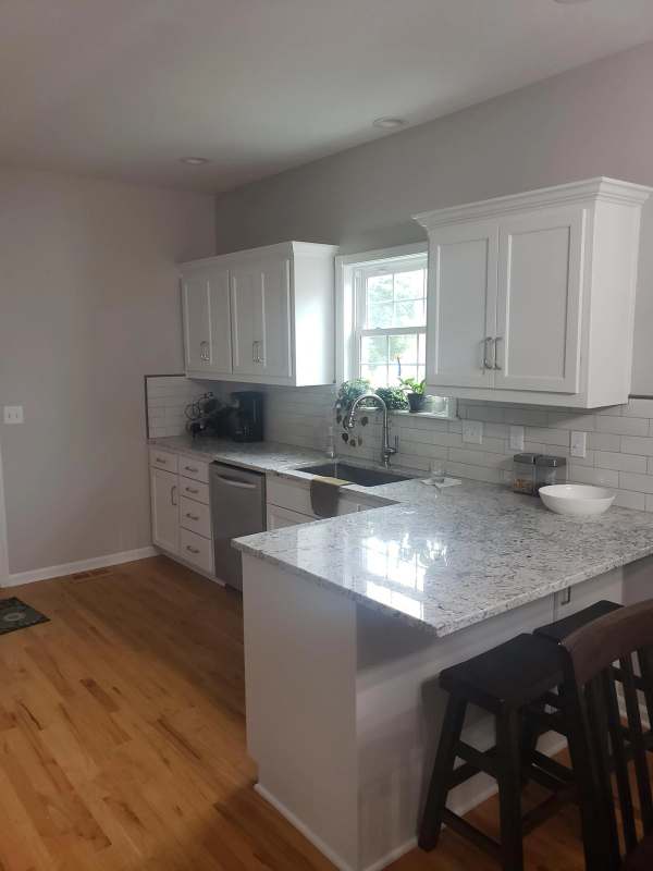The updated kitchen in Eudora, Kansas, with white painted cabinet doors, granite counters, a peninsula with seating & a white subway tile backsplash