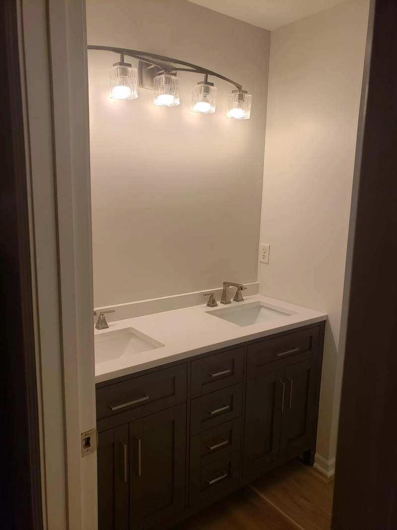 Double vanity with a white top & dark cabinet base under a four light fixture