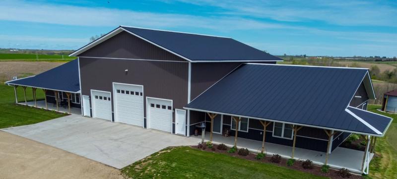 Barndominium with a wraparound covered porch, three garage bays, and a dark metal roof on open acreage