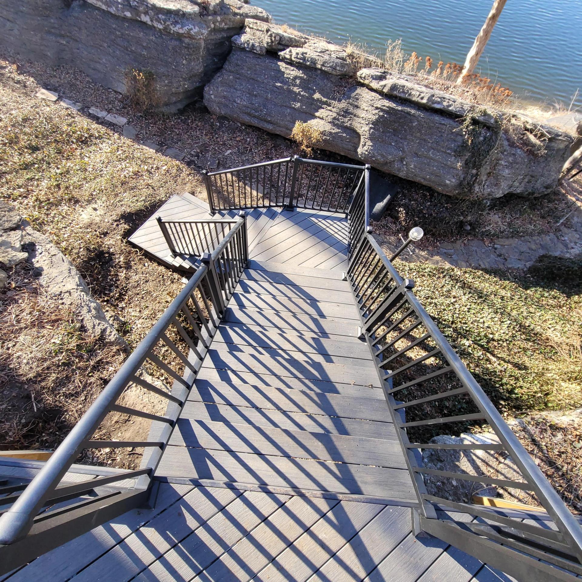 The composite stairway with black aluminum rails running down a limestone bluff to the lake landing in Lee's Summit, Missouri