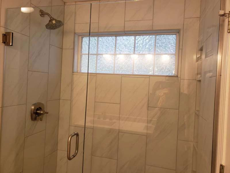 The master bath walk in shower with large format tile, a frameless glass door & a glass block window
