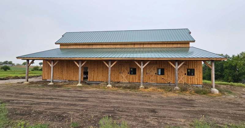 The covered porch running the full length of the elevation, carried on timber posts with the metal roof above