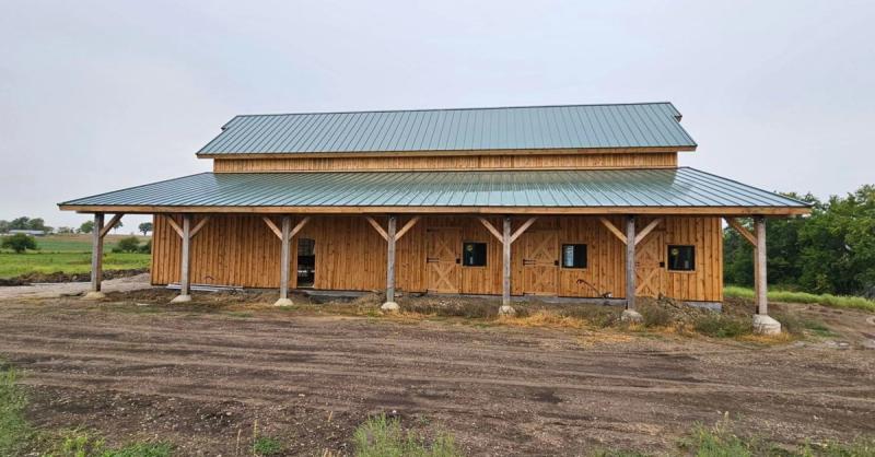 The full length covered porch of the Paola barndominium, carried on timber posts under a metal roof