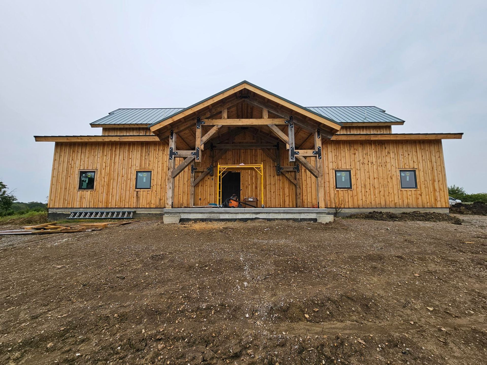 The finished barndominium in Paola, Kansas, seen straight on: heavy timber entry truss, vertical timber cladding & a standing seam metal roof