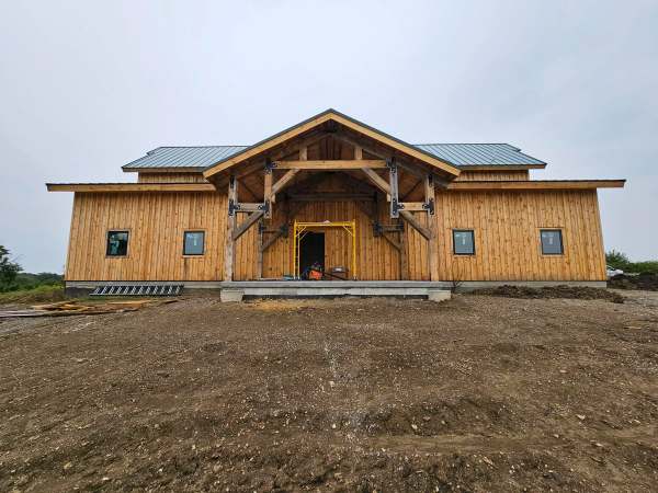 The finished barndominium in Paola, Kansas, seen straight on: heavy timber entry truss, vertical timber cladding & a standing seam metal roof