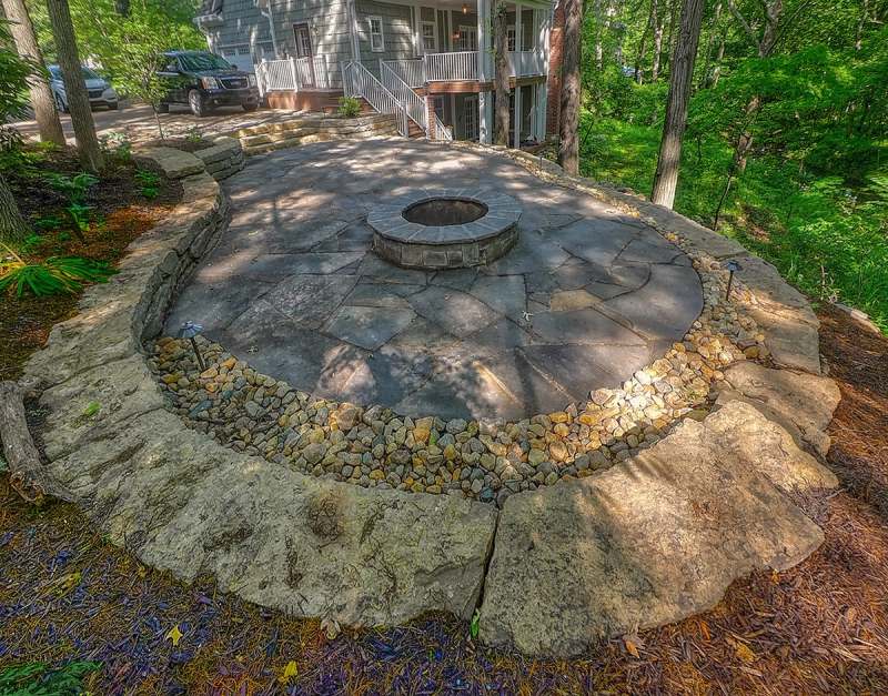 The round patio & fire pit, edged in river rock & held by a curved limestone wall