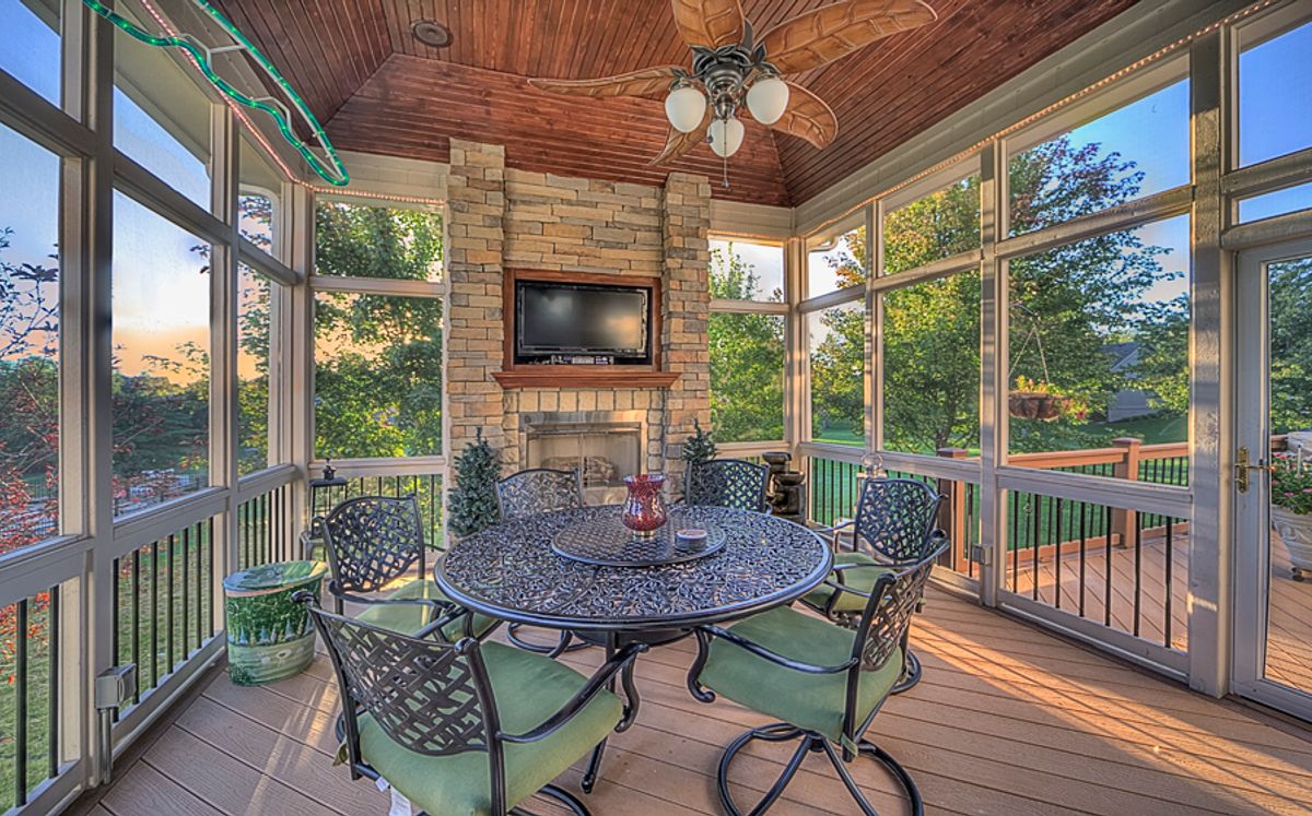 Screened porch with stone fireplace and tongue-and-groove ceiling at dusk — All Under One Roof, Kansas City
