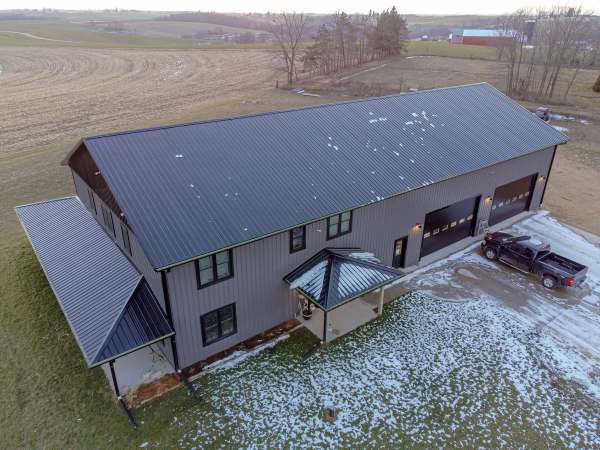 Two story barndominium with dark metal siding, a standing seam roof, and two oversized shop bays built by All Under One Roof