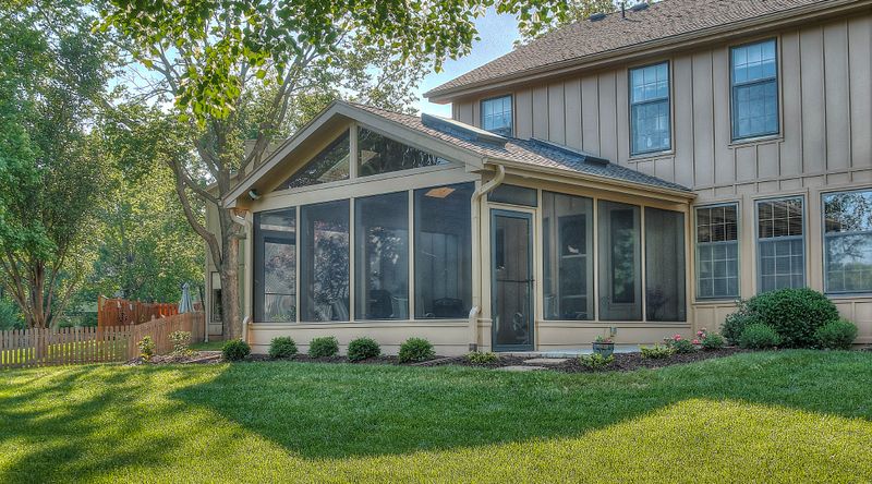 Three season room addition with wide windows overlooking a level backyard
