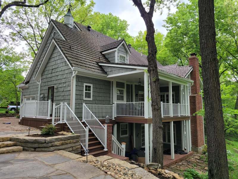 The rear of the house after the deck & porch rebuild, with white rails, a stair down to the patio & new limestone walls