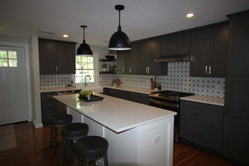 The remodeled kitchen in Prairie Village, Kansas: a quartz island with seating under black dome pendants, charcoal shaker cabinets & a patterned tile backsplash