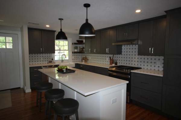 The remodeled kitchen in Prairie Village, Kansas: a quartz island with seating under black dome pendants, charcoal shaker cabinets & a patterned tile backsplash