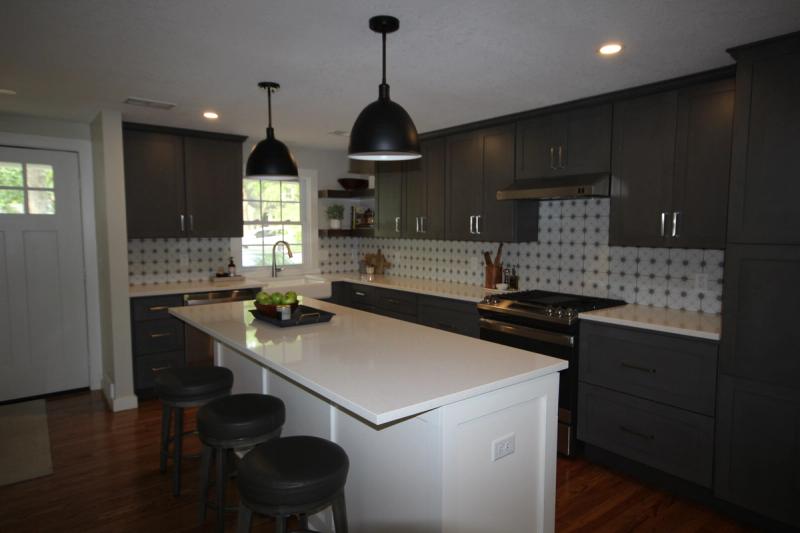 The remodeled kitchen in Prairie Village, Kansas: a quartz island with seating under black dome pendants, charcoal shaker cabinets & a patterned tile backsplash