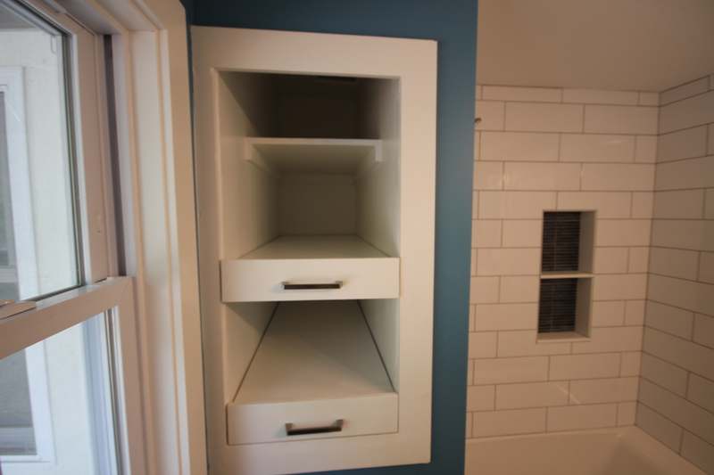 Recessed shelving with pull out drawers built into the bath wall beside the window