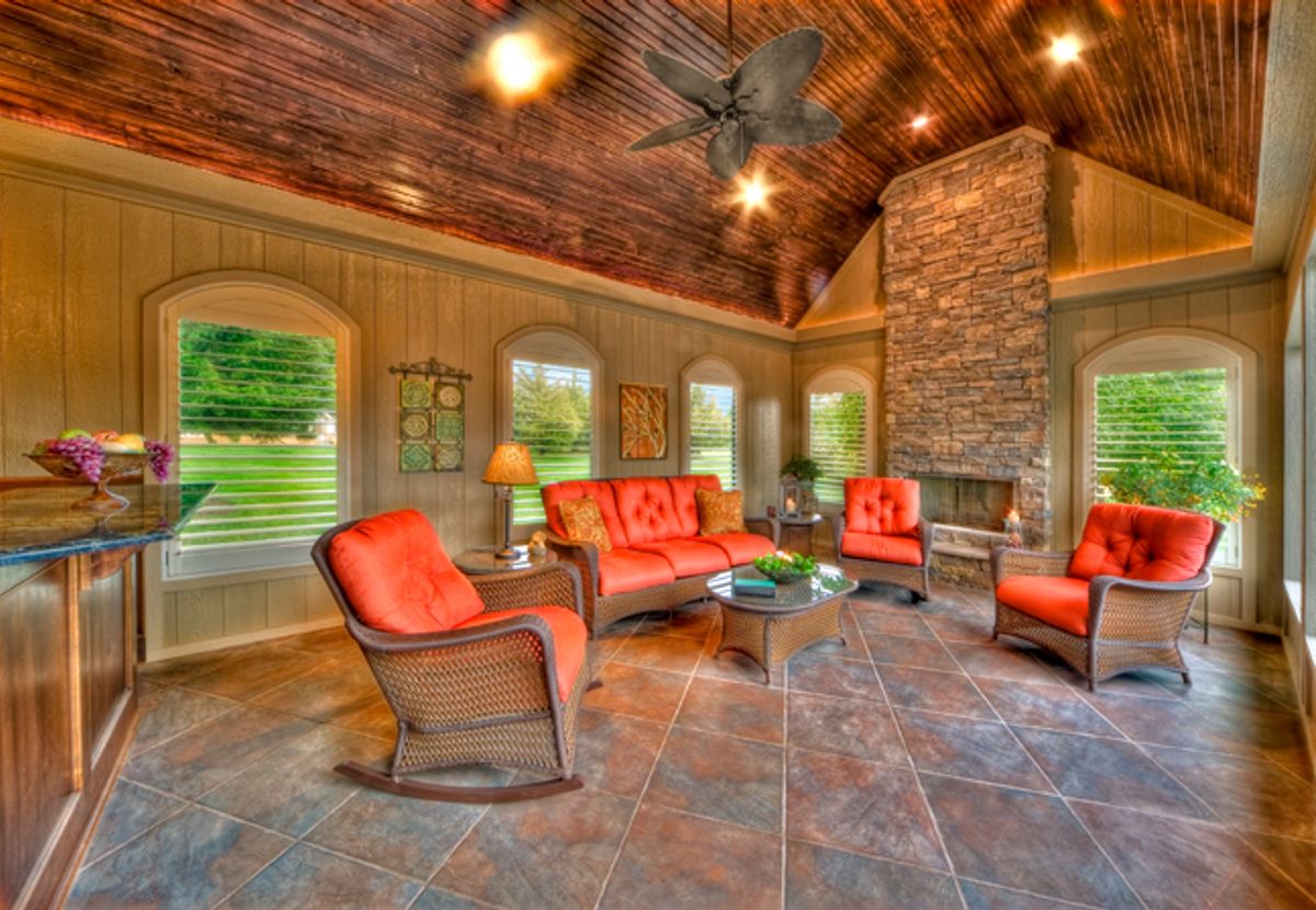Interior of a sunroom by All Under One Roof with a stone fireplace, tile floor and windows on all sides, Kansas City