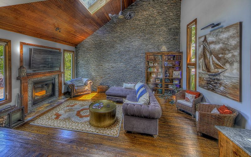 Living room with a stone fireplace and a stained wood plank ceiling after a whole home remodel