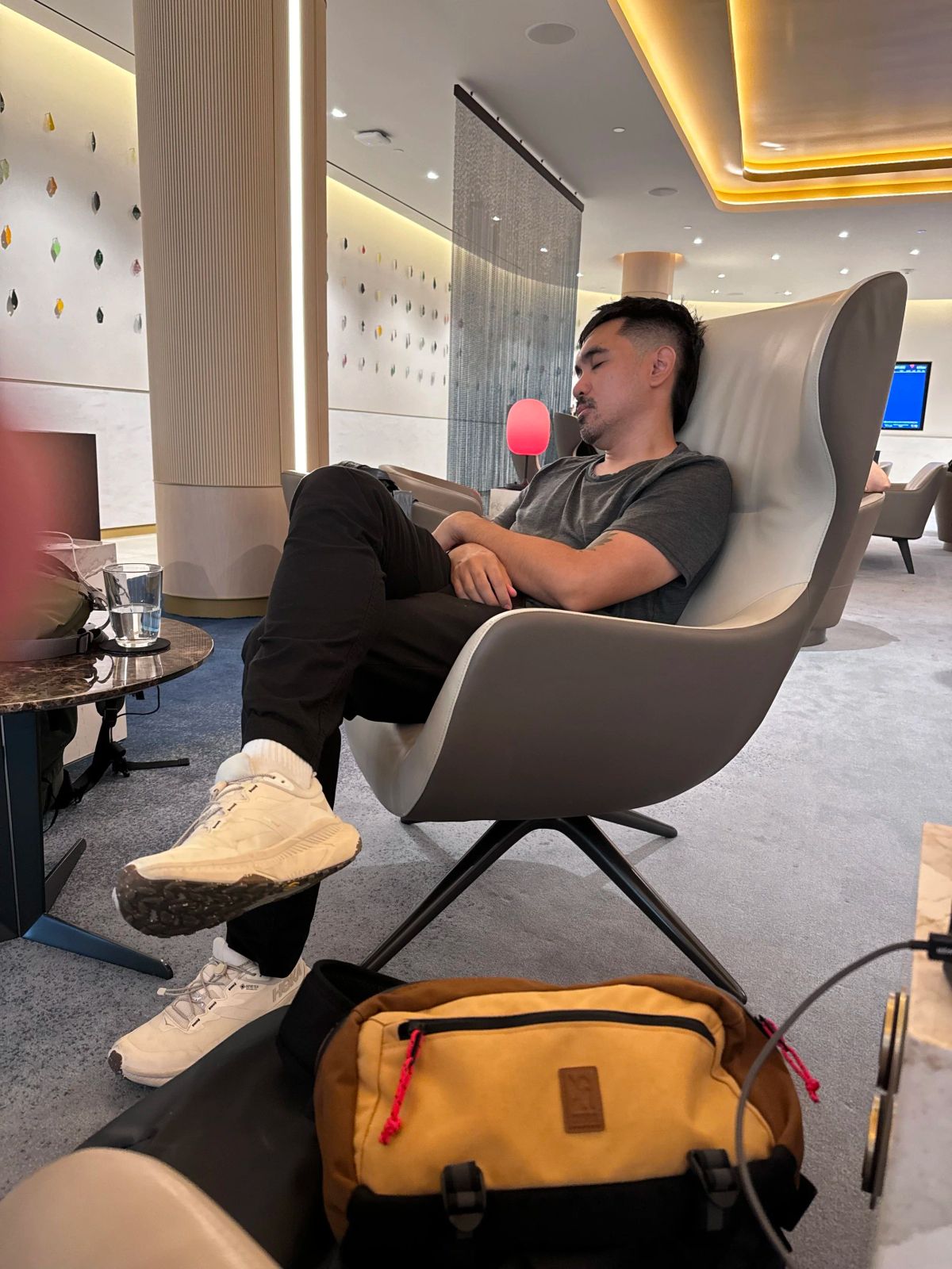 A man naps with his arms crossed in a curved chair in an airport lounge at JFK