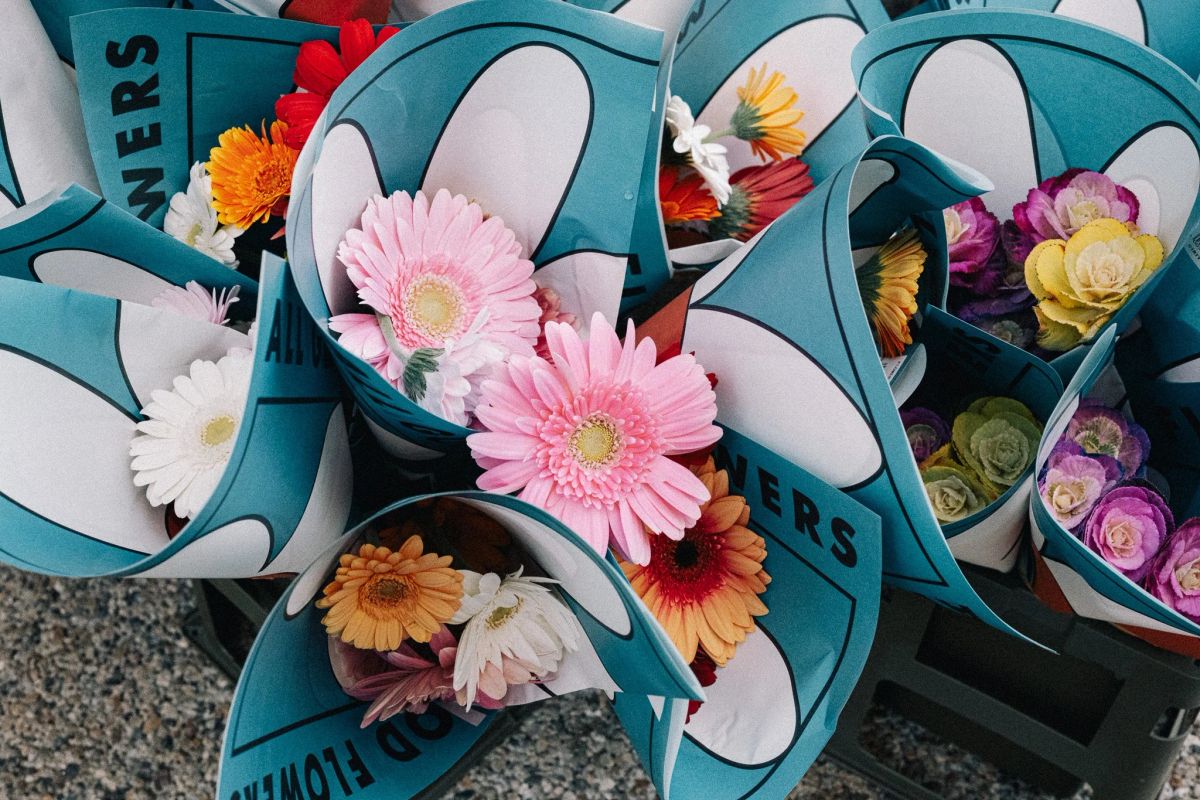 Bouquets of pink gerbera daisies, orange blooms and ornamental cabbages wrapped in teal paper cones