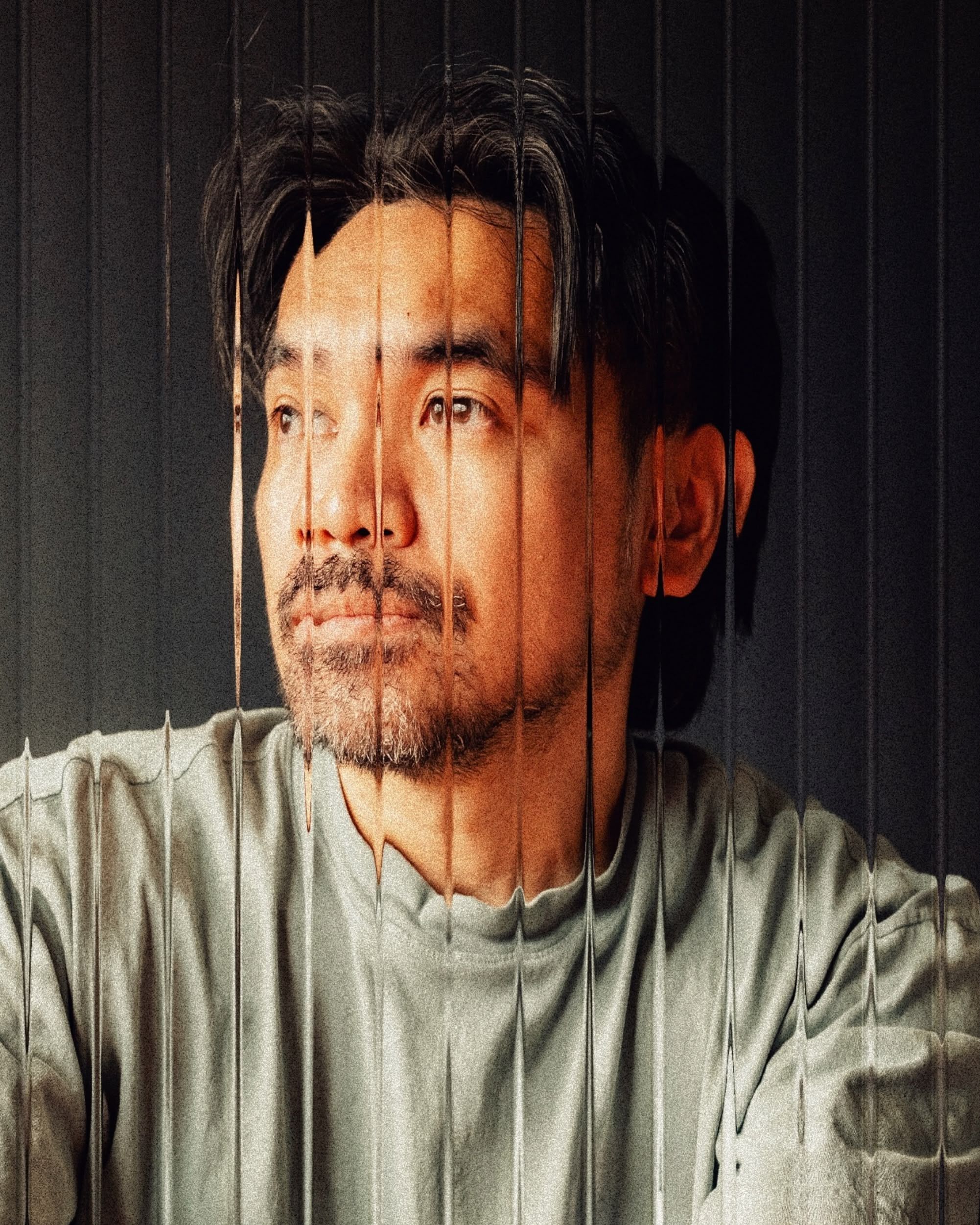 Mark Dean Guillermo in a grey T-shirt, looking off to the side, photographed through ribbed glass