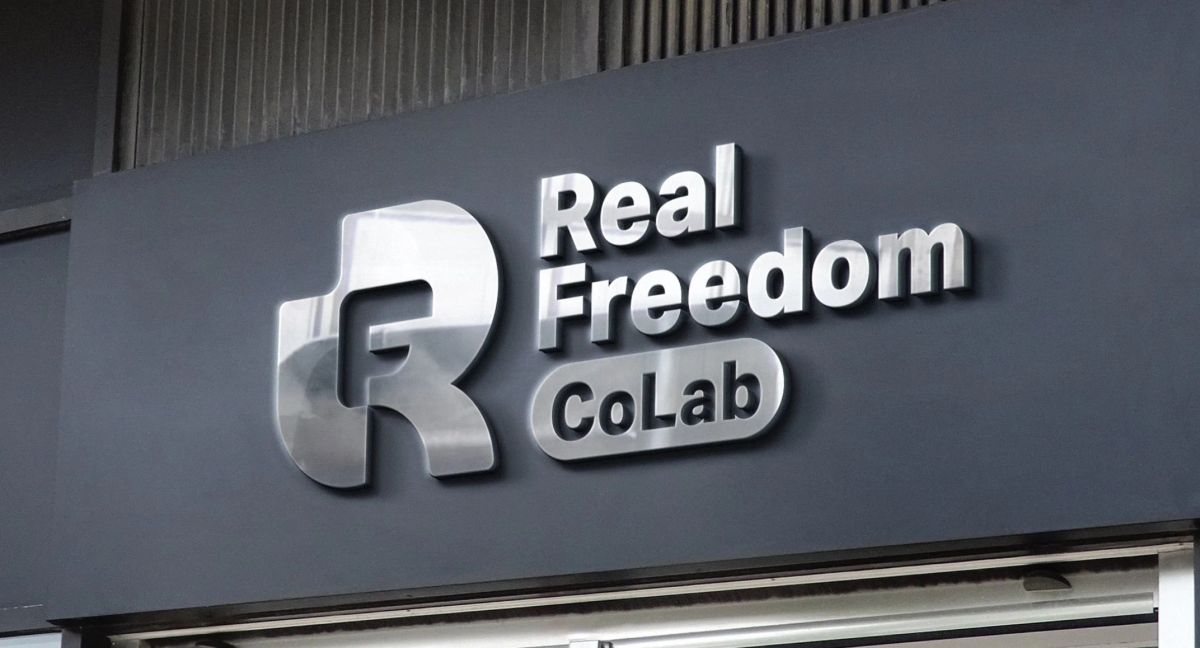 Real Freedom CoLab monogram logo rendered as brushed metal storefront signage mockup