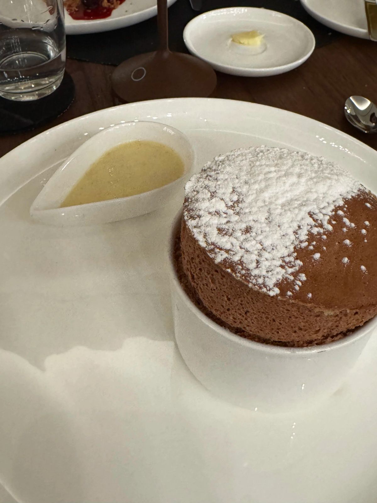 A chocolate soufflé dusted with powdered sugar, served with a small dish of vanilla sauce