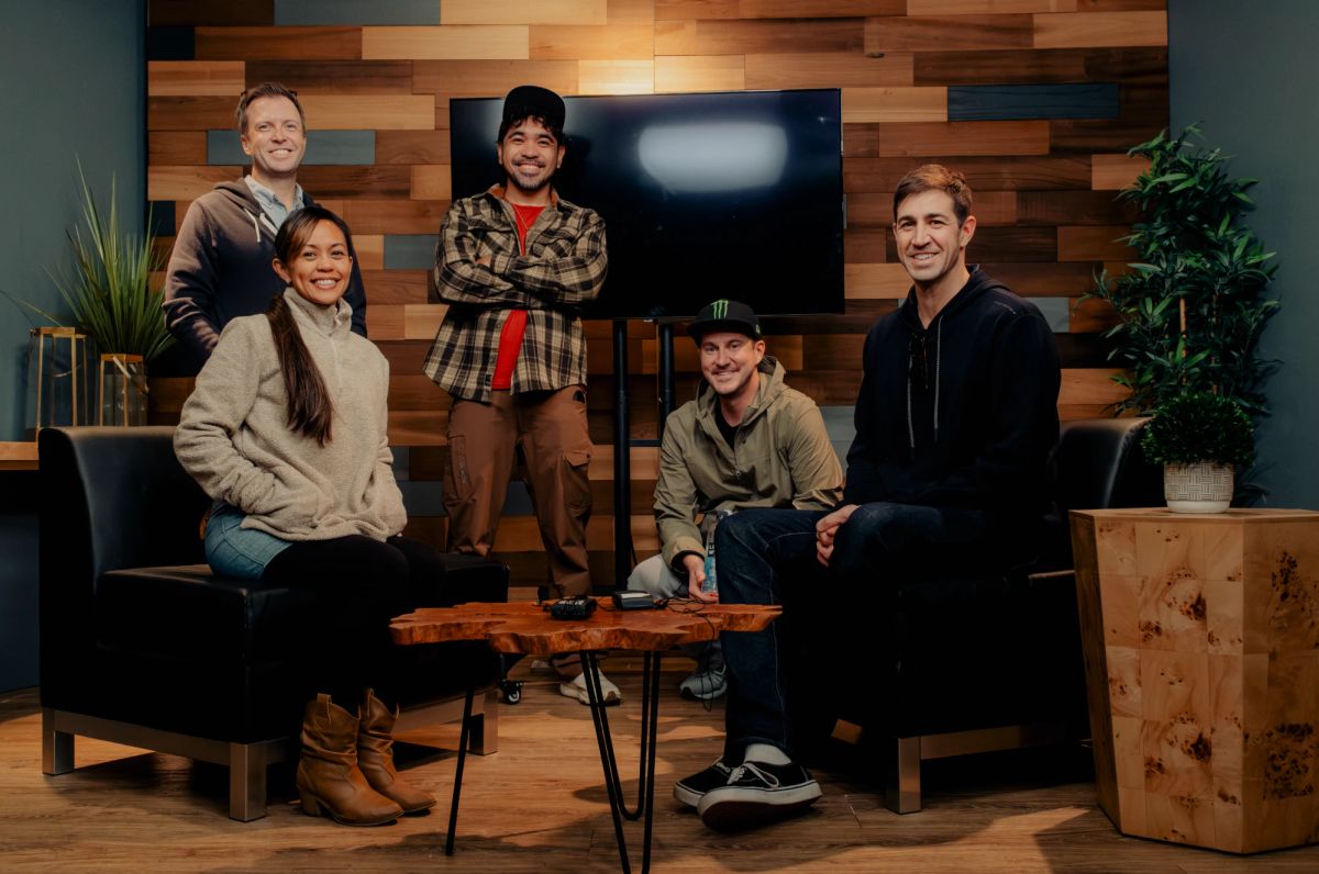Five people from the shoot posing on the studio set in front of a reclaimed-wood wall, with leather chairs and a live-edge coffee table