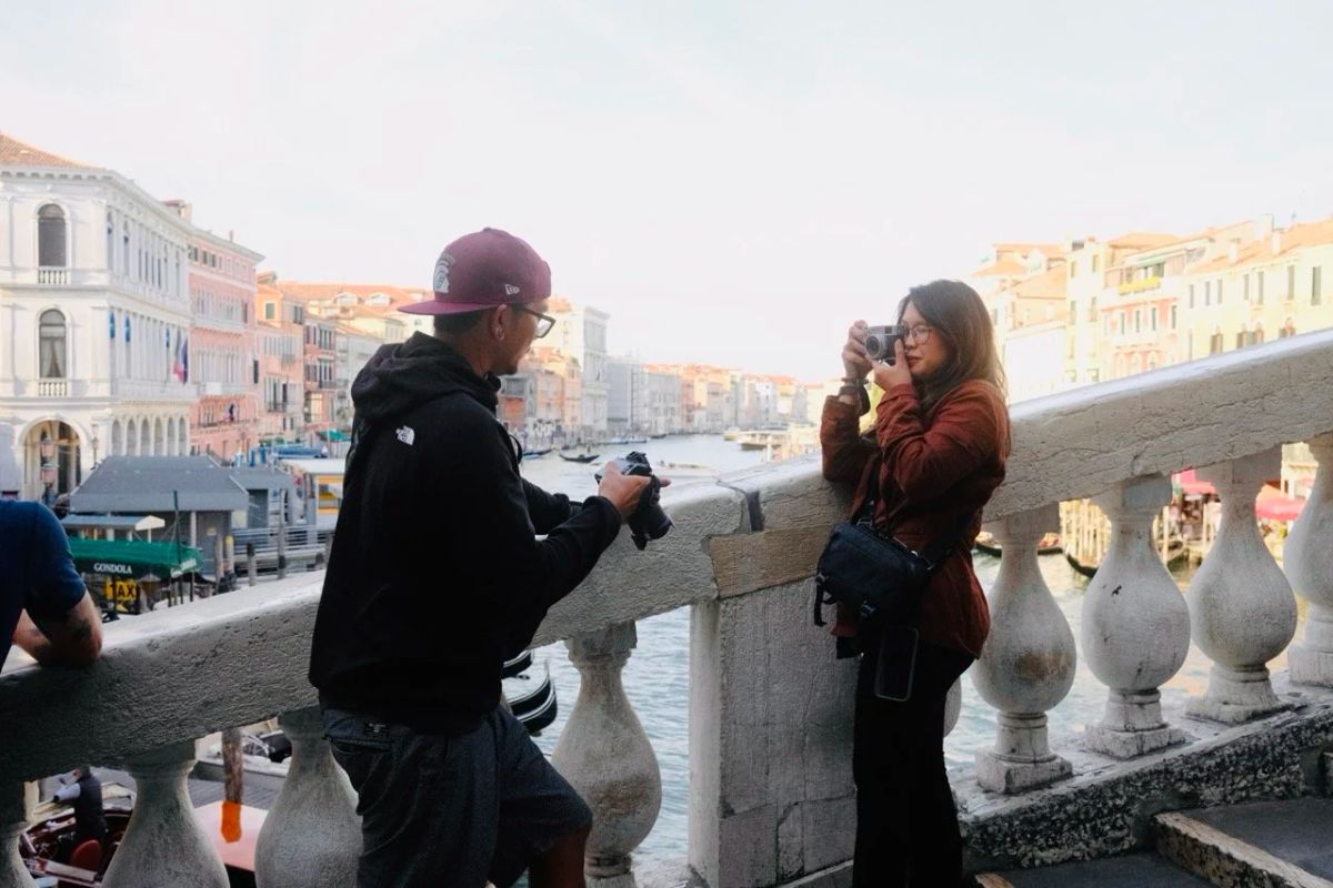 A man and a woman photograph the Grand Canal from a stone bridge balustrade in Venice