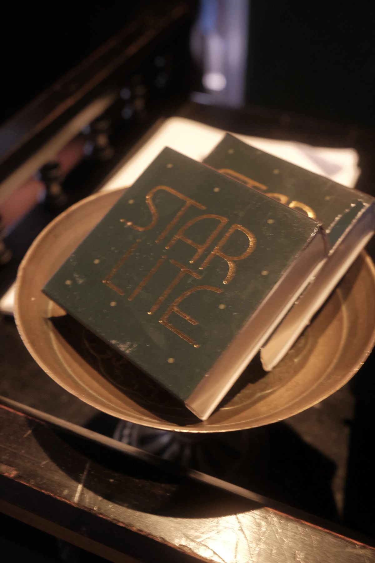 Two dark green books stamped with gold "Starlite" lettering resting in a brass dish on a bar