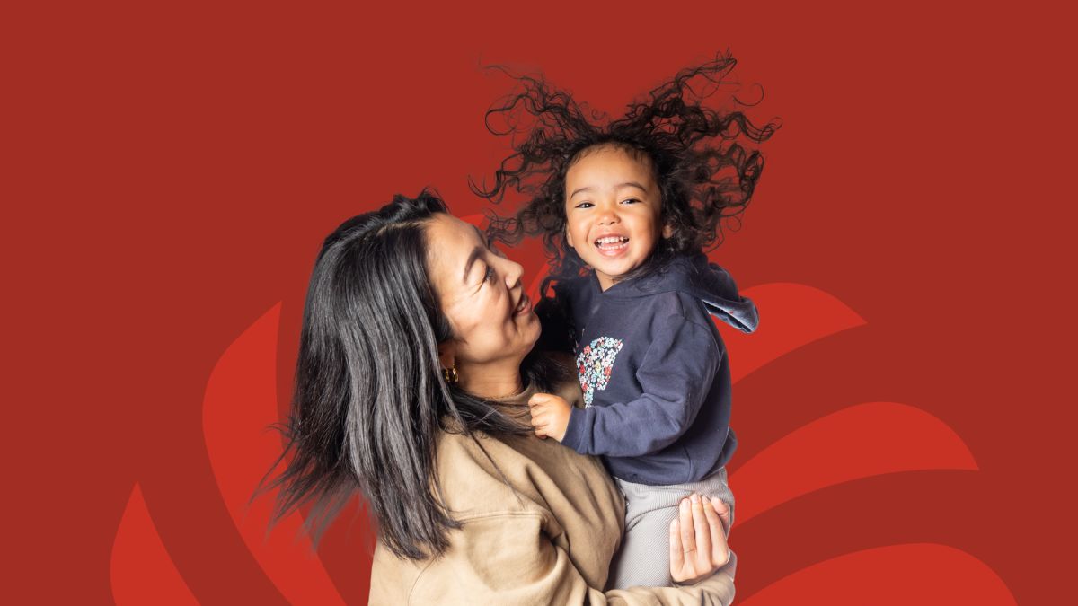 Laughing woman lifting a curly-haired child against a red HawaiiUSA background with a curved brand pattern